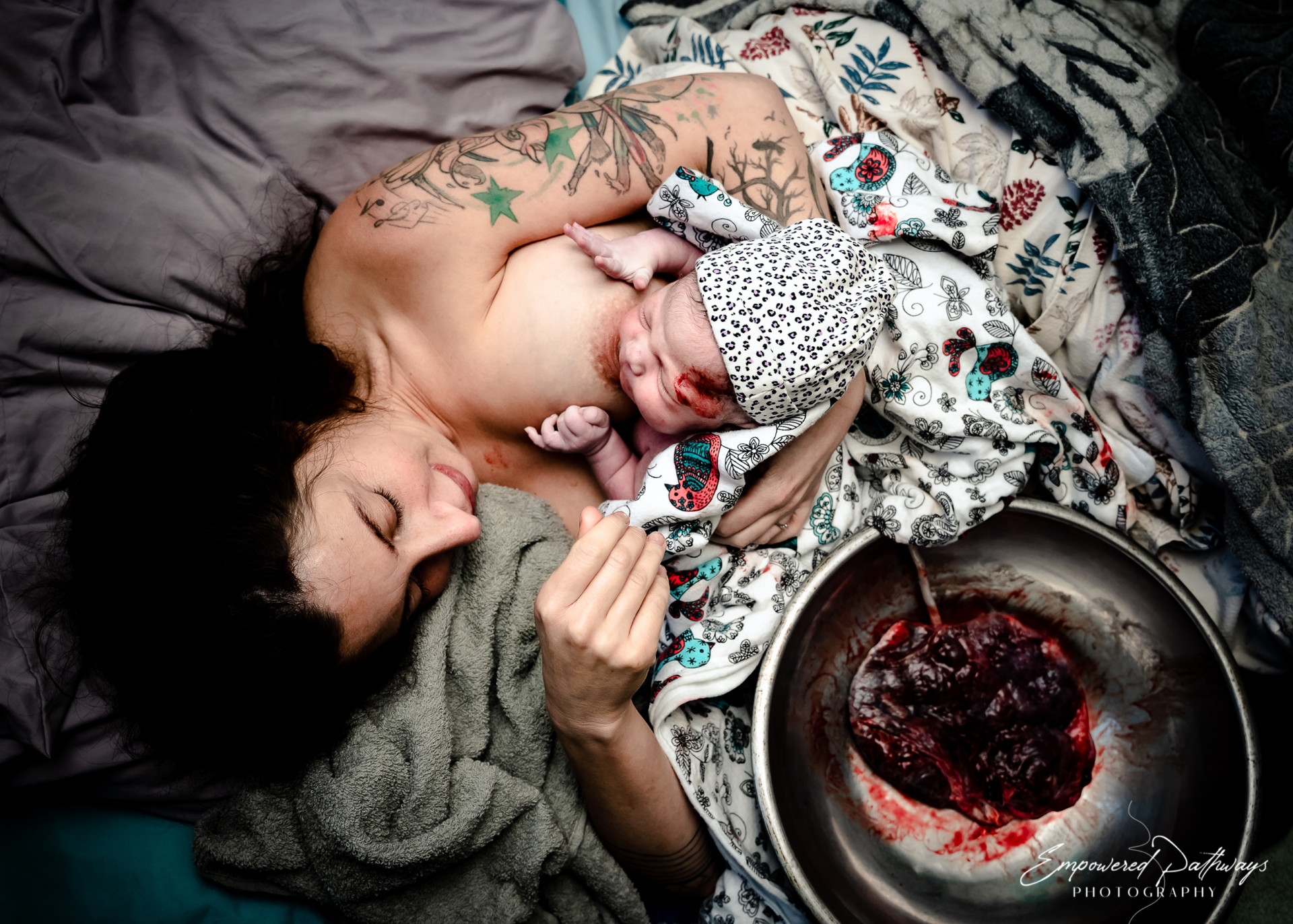 Une femme allongée dans un lit avec le placenta dans un bol à côté d'elle, allaite son nouveau-né
