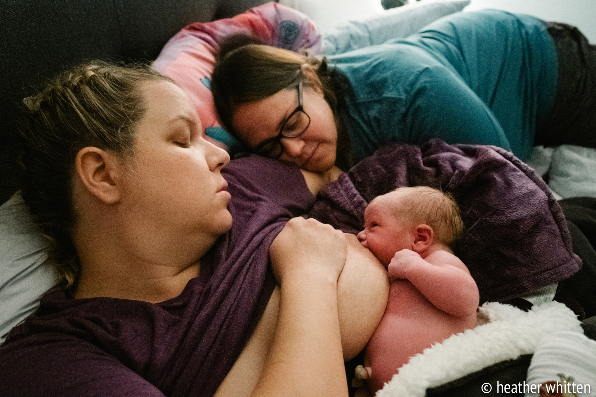 Deux mère allongées sur un lit, l'une allaite un nouveau-né