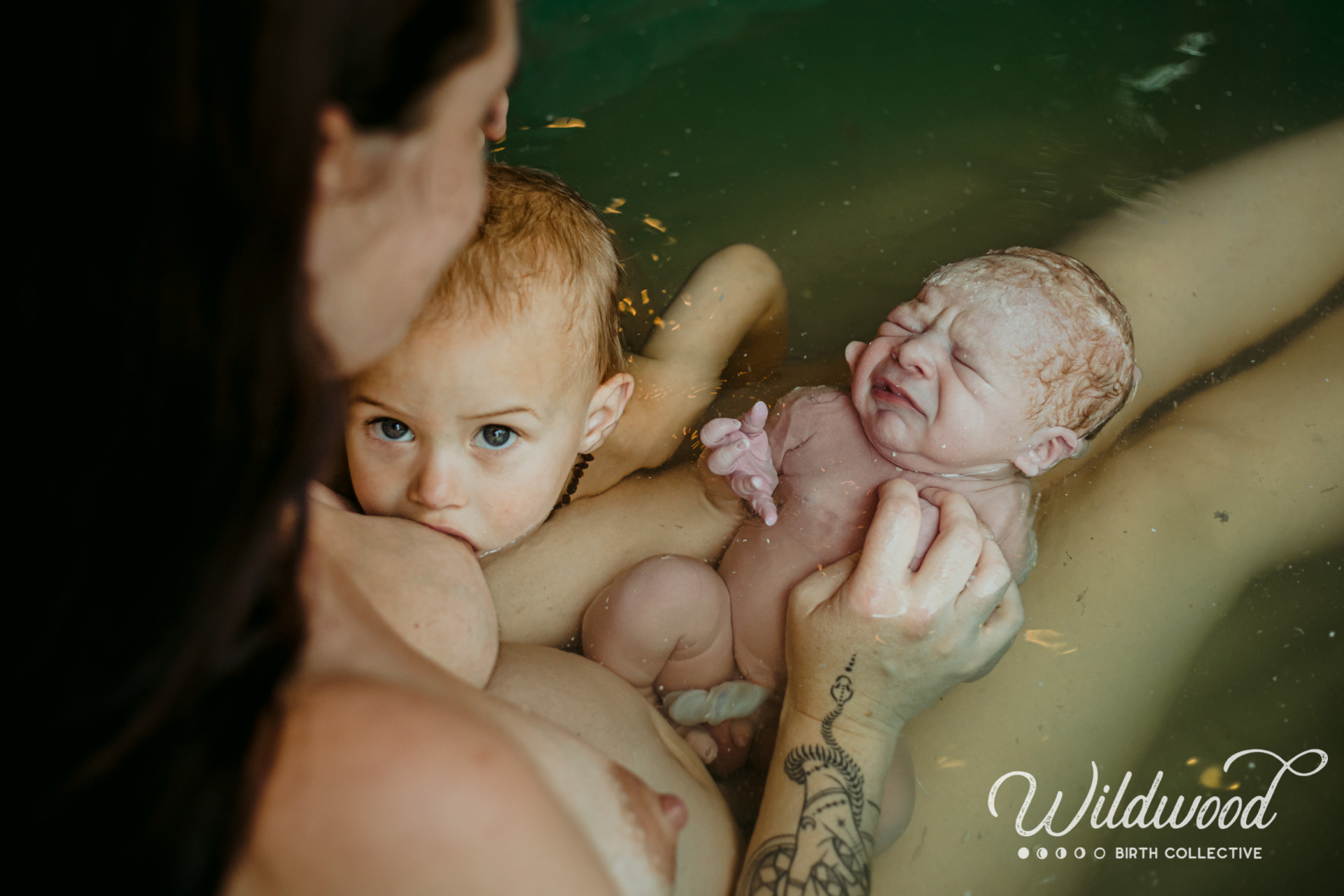 Une mère allongée dans une baignoire allaite tient son nouveau né sur les jambes et allaite son autre enfant